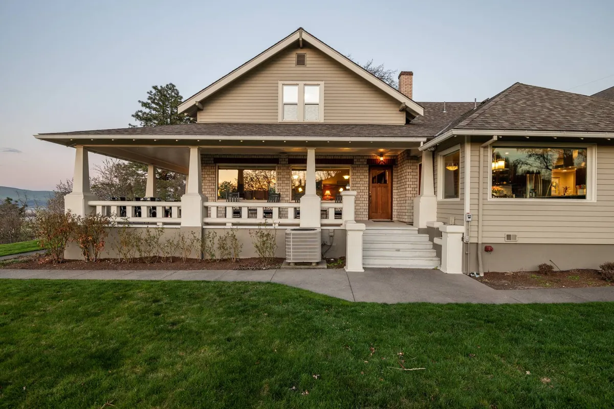 A welcoming view of the front porch with large windows and a landscaped lawn, bathed in sunset light. This image captures the ambiance of enjoying outdoor gatherings, watching sunsets, and relaxing after action-filled days.