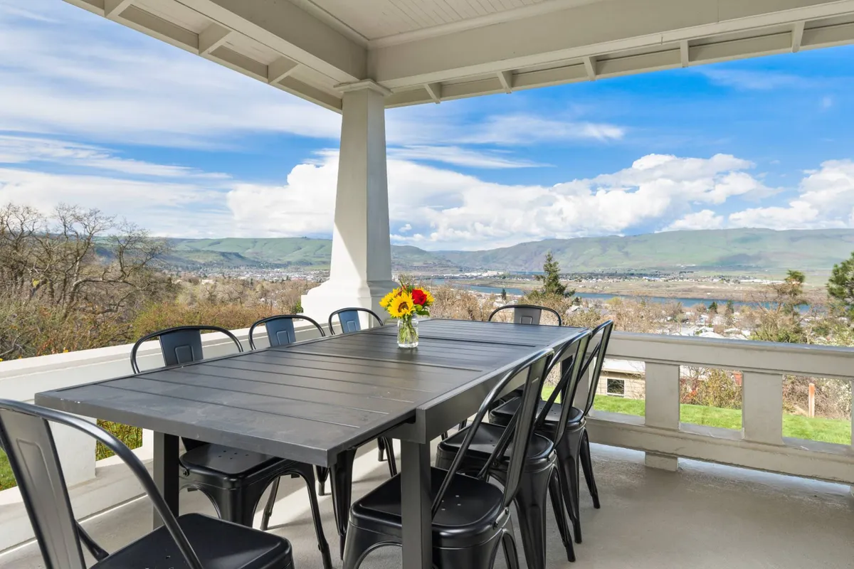 This image showcases a large outdoor dining table adorned with a vase of flowers, positioned to take in a scenic view. The setting radiates a cheerful and relaxed mood, ideal for hosting group meals, enjoying the sunrise or sunset, and socializing outdoors.