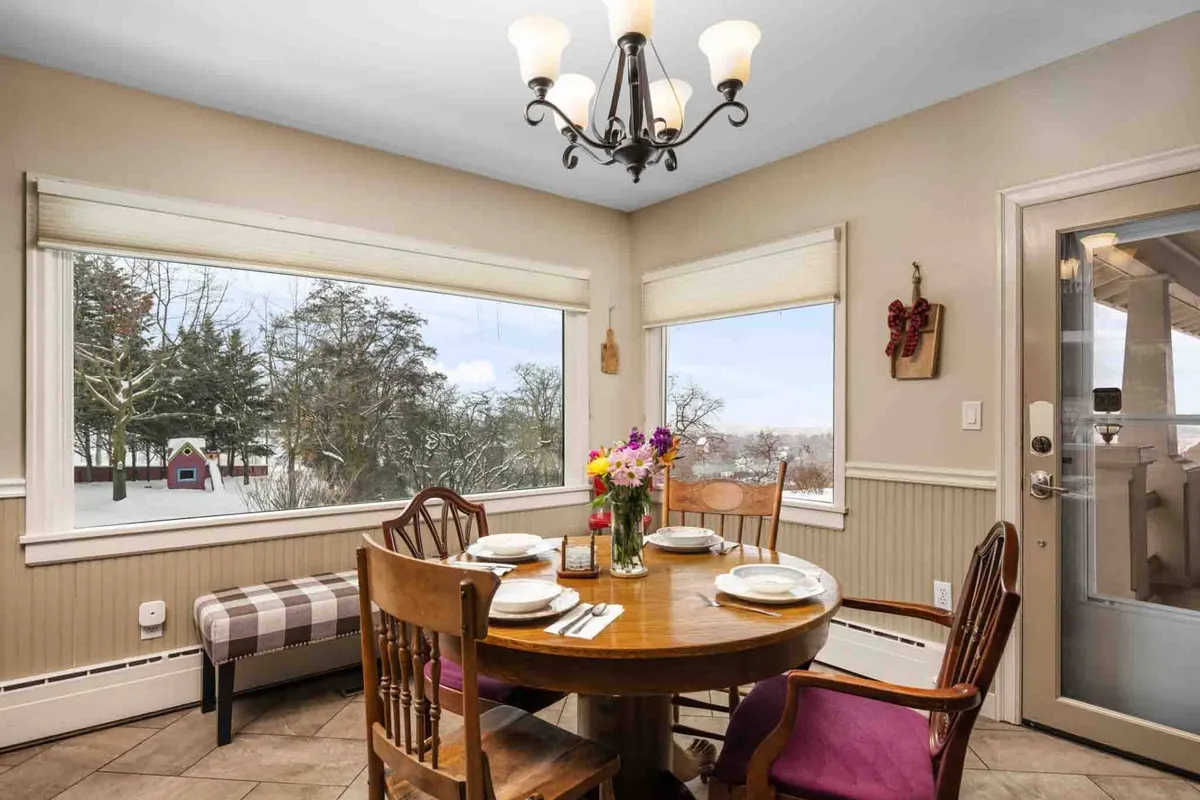 A warm, inviting dining area with a wooden table set for a family meal, flowers in a vase as a centerpiece, and large windows allowing soft natural light to stream in. The chandelier adds a touch of elegance, while the decorative wall elements create a cozy, homelike atmosphere. The expansive windows offer scenic views, reinforcing a tranquil connection to the outdoors.