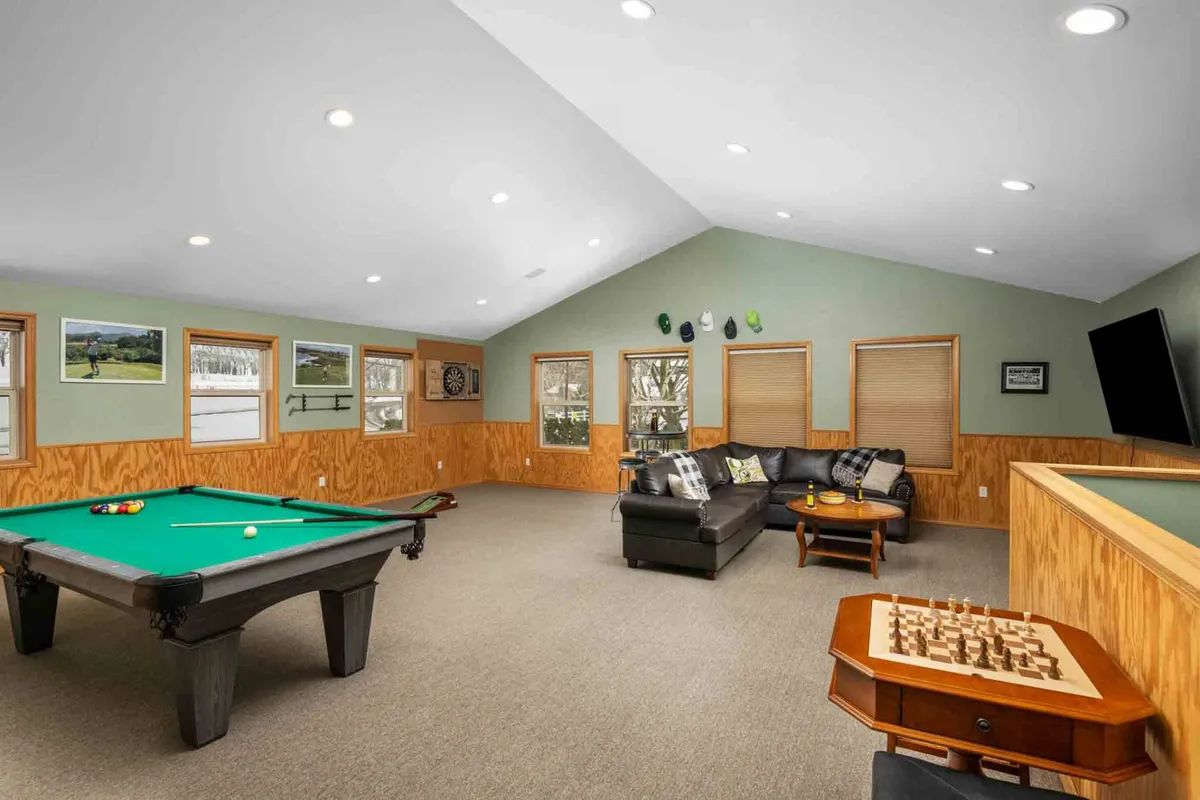 The entertainment lounge is depicted with a pool table, a cozy sofa seating area, a chess table, and wall decor. The large streaming TV is visible, inviting movie nights or sports viewing. The setup is relaxed and ready for both active and leisurely fun.
