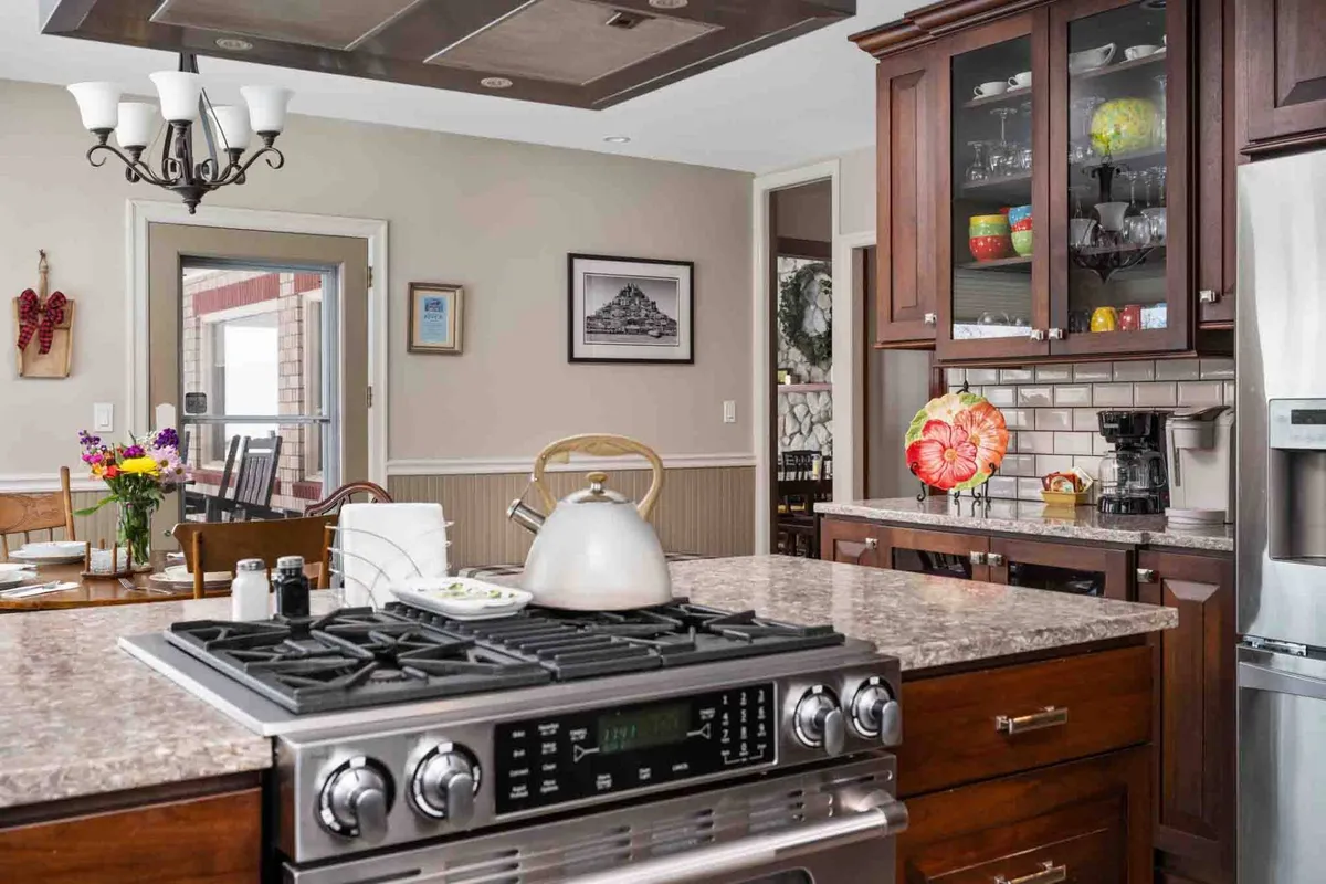 A chef’s kitchen with a central island, stainless steel stove, colorful dishware displayed in open cabinets, and a vibrant floral centerpiece. The design encourages culinary creativity and group meals, with plenty of space for guests to gather, snack, or converse while food is prepared.
