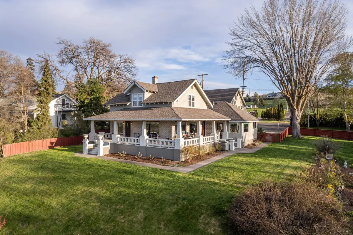 This inviting exterior image showcases the home's large front porch, expansive landscaped yard, and a unique architectural profile. The open green space and prominent tree in the yard suggest ample room for outdoor games, family gatherings, and relaxation in nature.