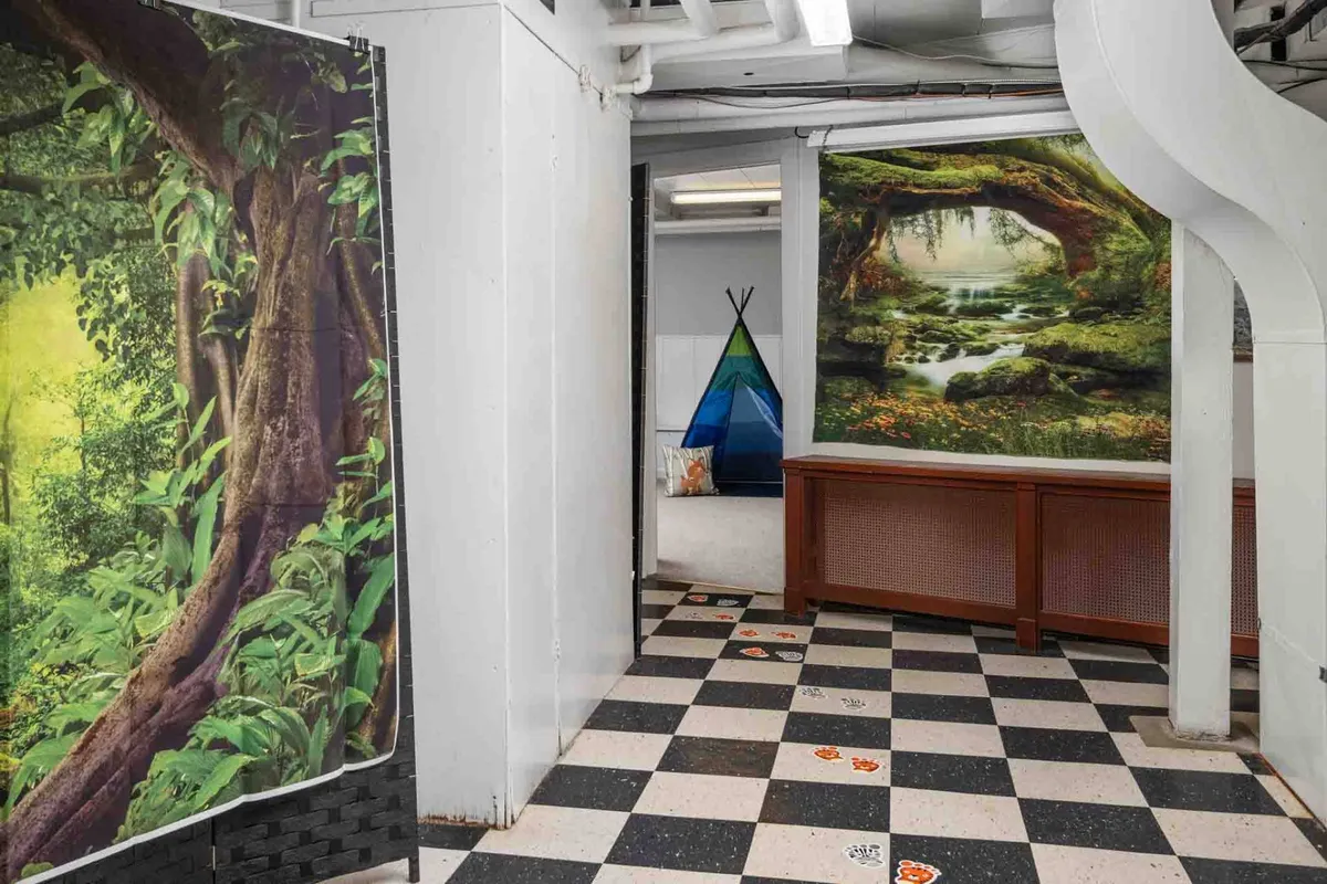 This playful children’s area features a vibrant nature-themed wall mural, a colorful teepee, and a checkerboard floor. The space is designed for creativity and imaginative play, perfect for younger family members to explore and have fun.