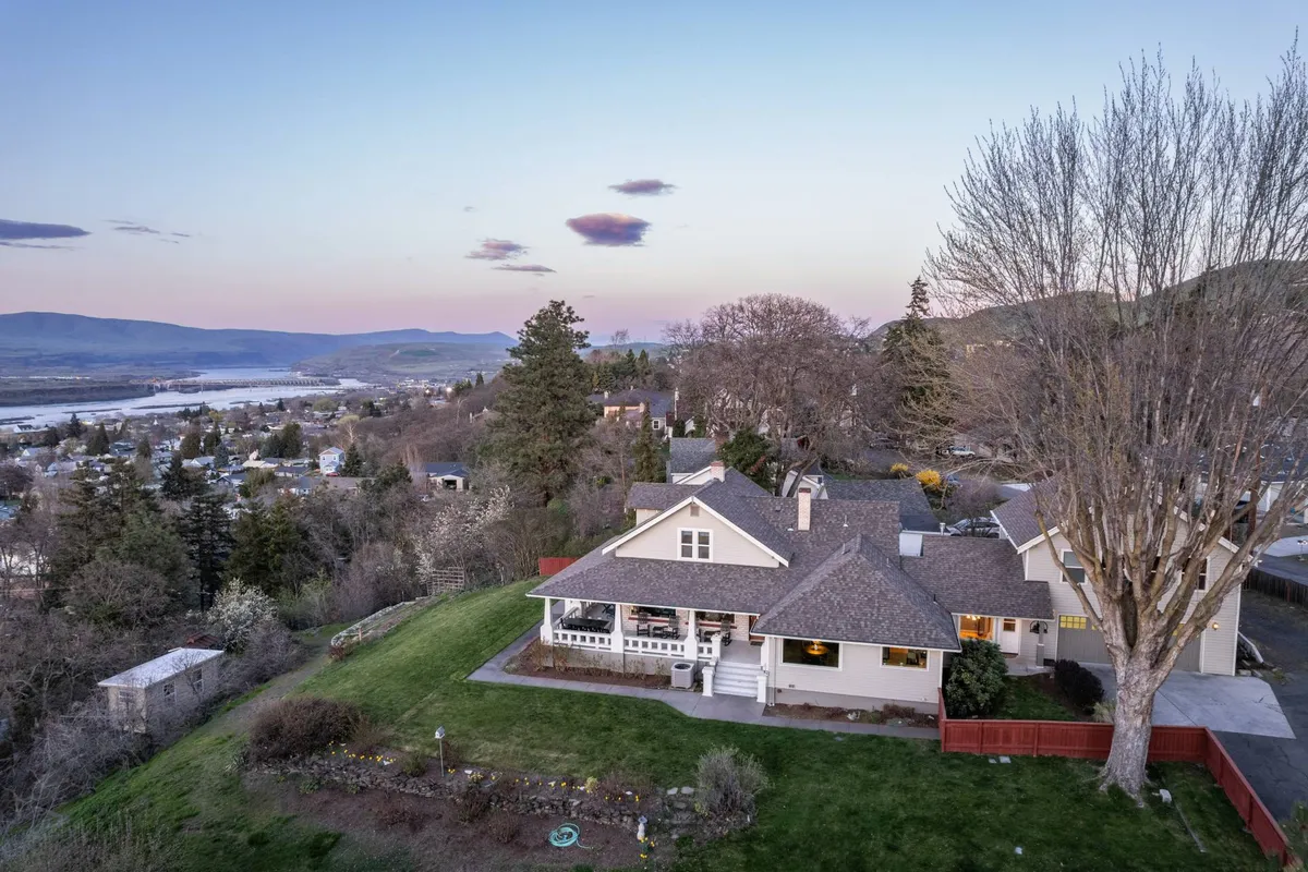 This image captures the spacious front porch of HillsHyde Escape surrounded by manicured lawns, mature trees, and an expansive view of the valley. The porch invites relaxation and offers a vantage point to take in the scenic outdoors, making it an ideal setting for unwinding after a day of adventure.