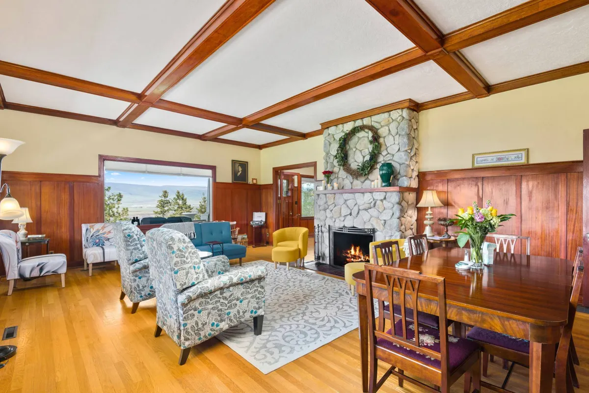 A cozy, sun-drenched living and dining area anchored by a classic fireplace. The inviting seating area surrounds a dining table suitable for gatherings, while the warm light streaming in through large windows illuminates the space. Hints of vintage charm blend with updated comfort, capturing the heart of this home's communal spaces.