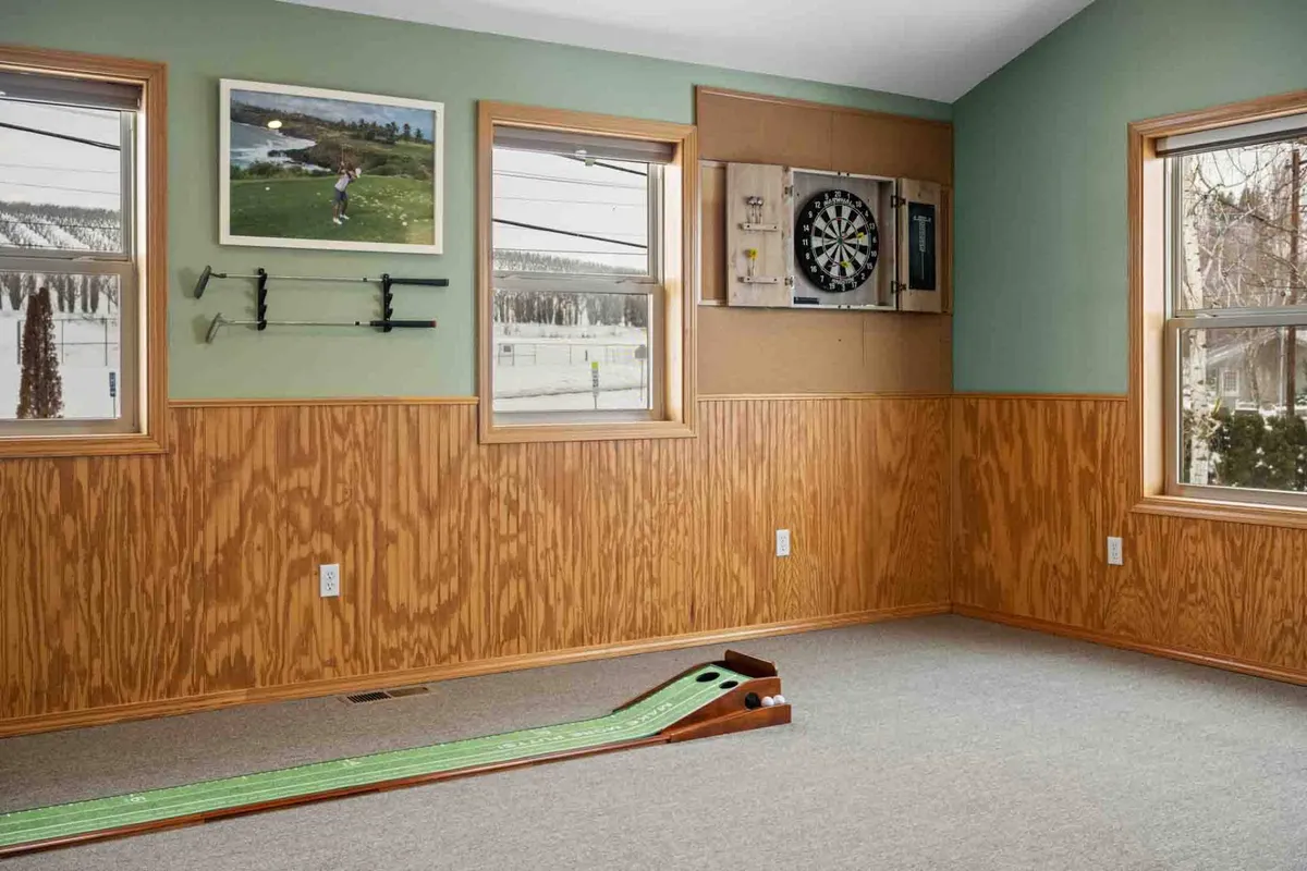 An interior entertainment space featuring a golf putting green, dartboard, and framed photographs. The area exudes a playful, relaxed atmosphere ideal for friendly competitions, games, and shared family experiences.