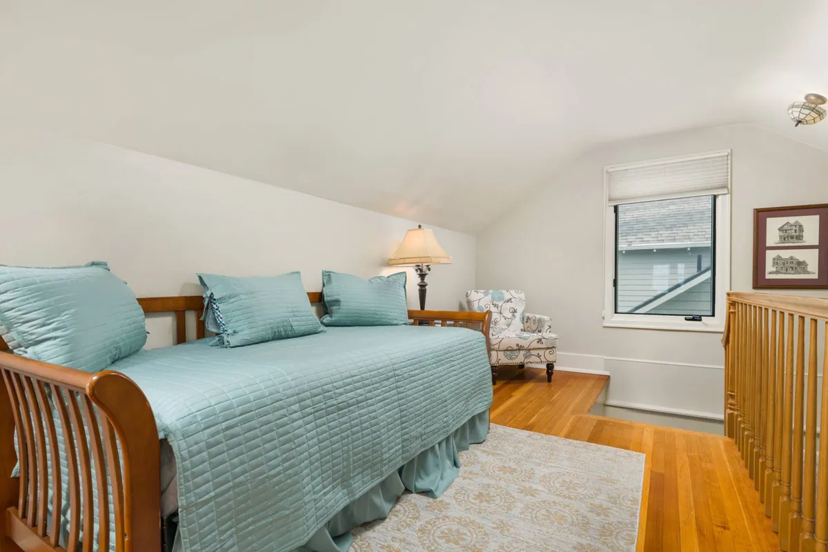 The image displays a daybed tucked into a sunny, inviting alcove, complete with a lamp, accent chair, and window letting in natural light. The setting exudes comfort, perfect for a solo traveler or a child’s cozy retreat.