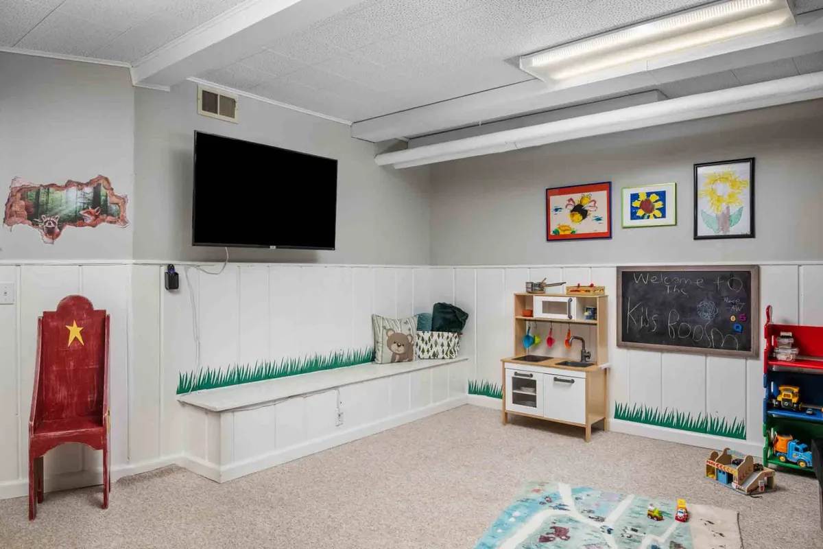 A joyful play space for kids, this image highlights a chalkboard with a welcoming message, toy storage, a colorful red chair, and a TV mounted on the wall. The setup encourages drawing, play, and screen time, all within a vibrant and safe environment.