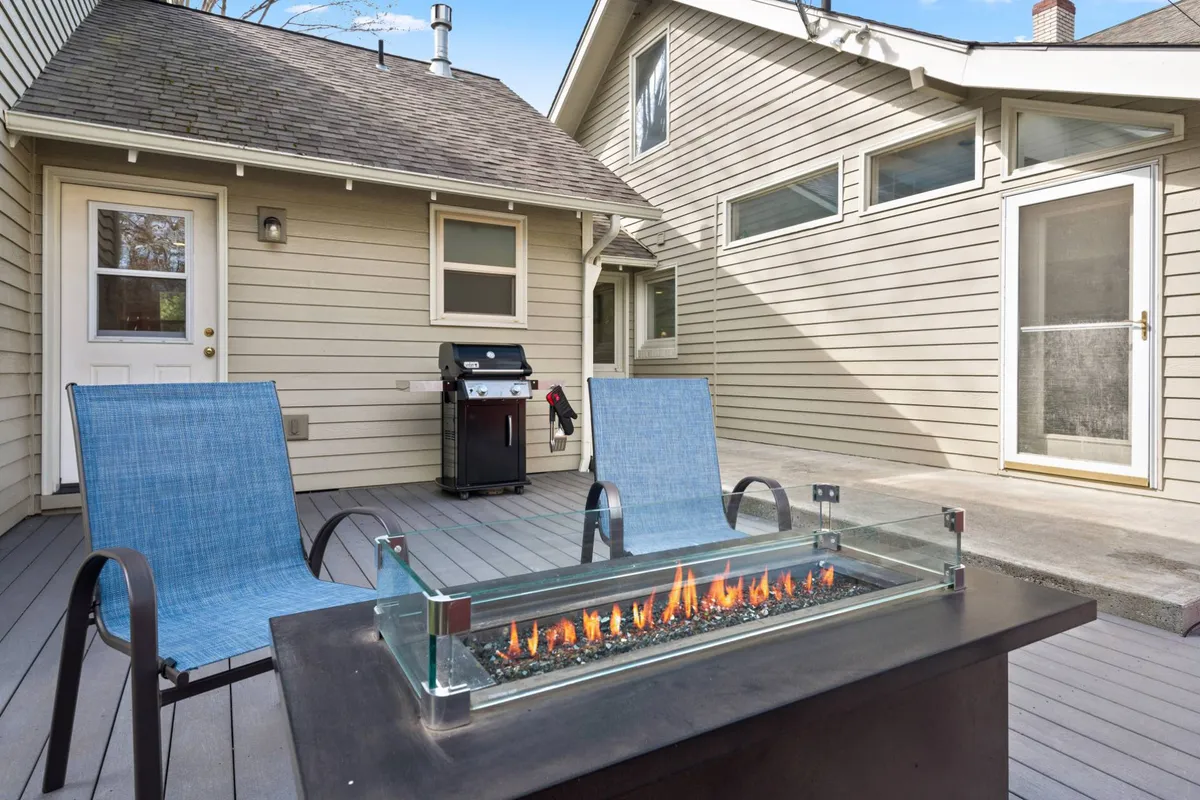 An inviting outdoor area with a fire pit surrounded by blue chairs and a grill ready for barbecues. The scene suggests a relaxed atmosphere for evening gatherings, laughter, and connection under the stars.
