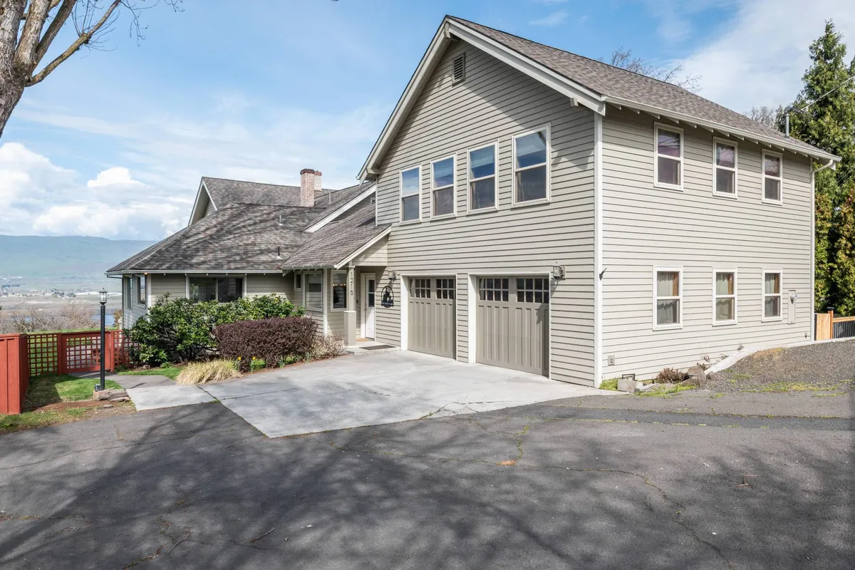 A welcoming exterior view of the house with a landscaped yard, inviting porch, and garage. The scene is bathed in warm sunset light, hinting at the serene and scenic setting of the home. The porch looks perfect for gathering friends and enjoying the end of the day together.
